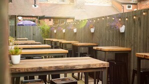A patio area with wooden tables and chairs, string lights, and potted plants. - Duke William Hotel (Lincoln)