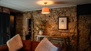 A cozy room with a stone wall, a wooden table with a vase and flowers, and a brown leather sofa with fluffy pillows. - Duke William Hotel (Lincoln)