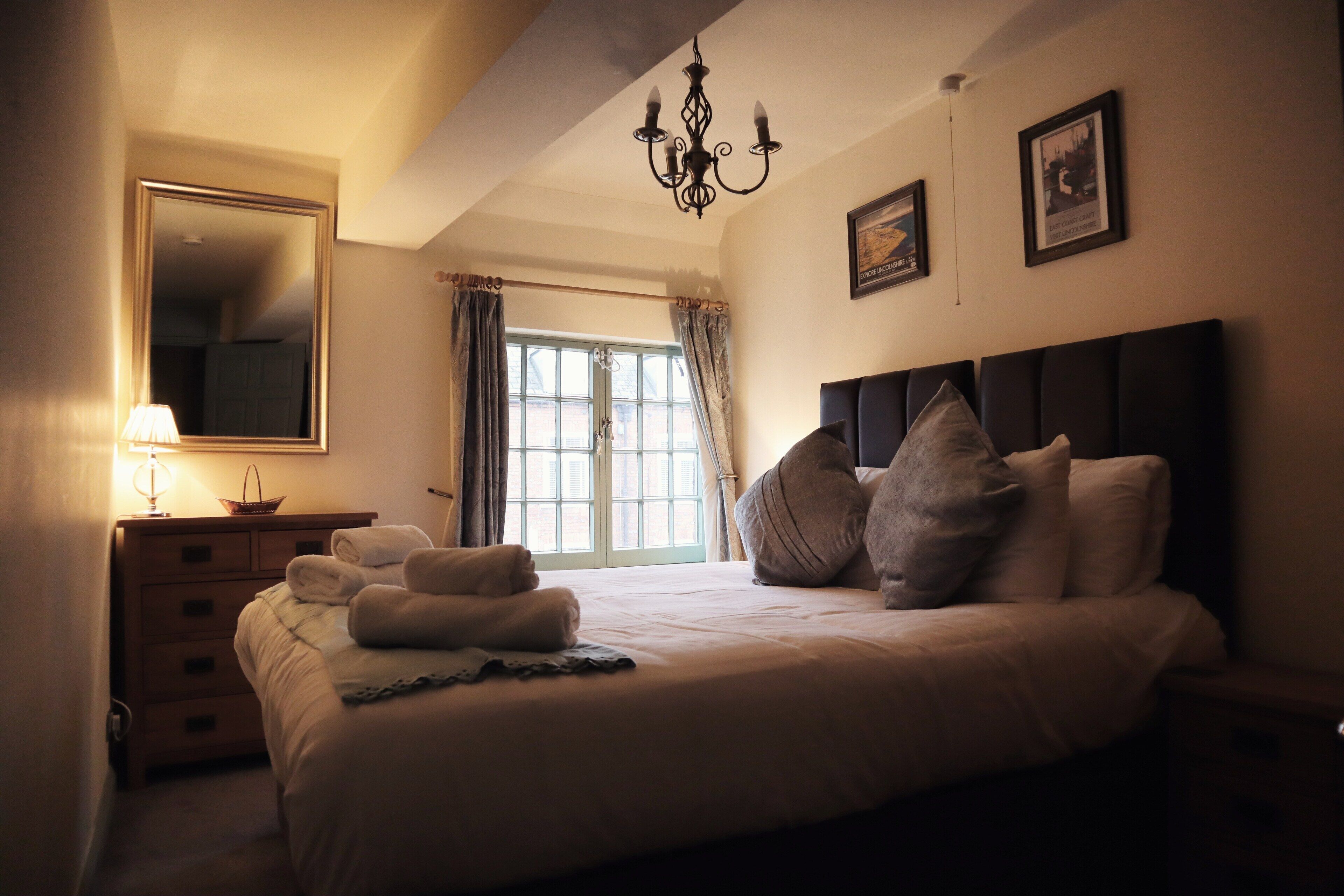 Une chambre à coucher avec un grand lit, une commode, un miroir et un lustre.