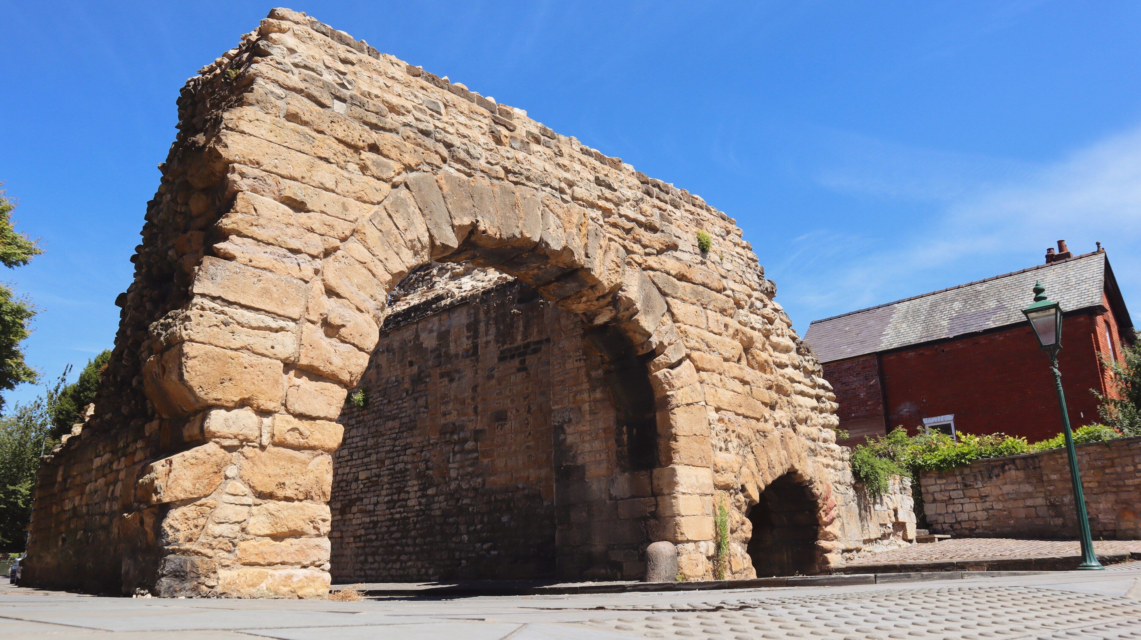 An ancient stone archway with a brick building in the background.