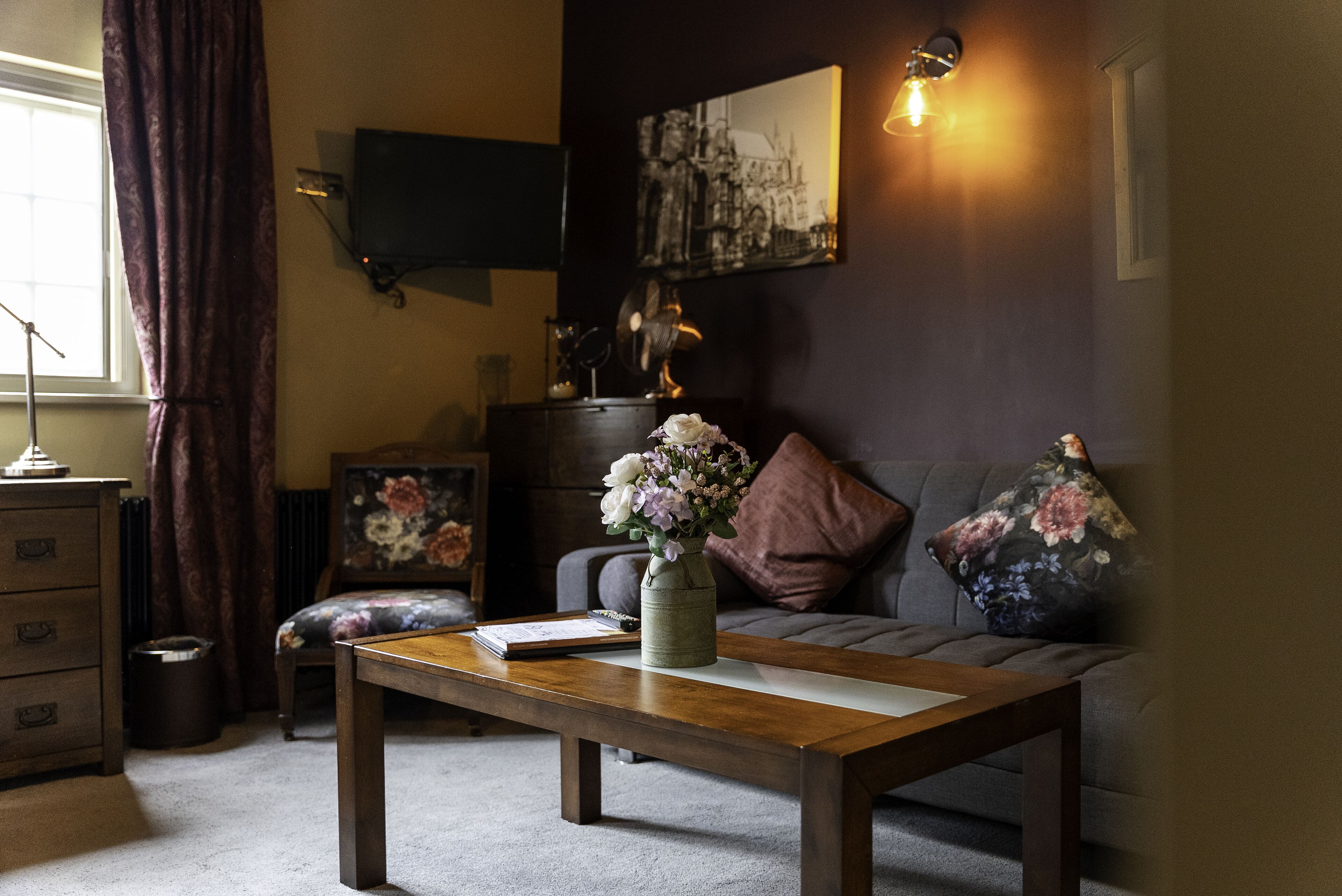 Un salon avec une table basse en bois, un canapé, un téléviseur fixé au mur et un tableau.