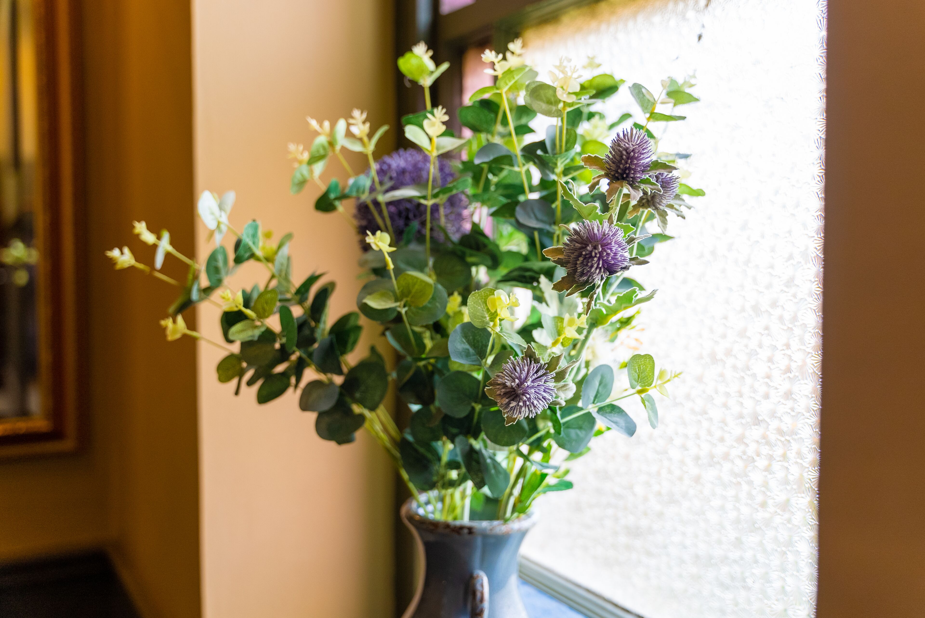 A potted plant with green leaves and purple flowers on a windowsill.