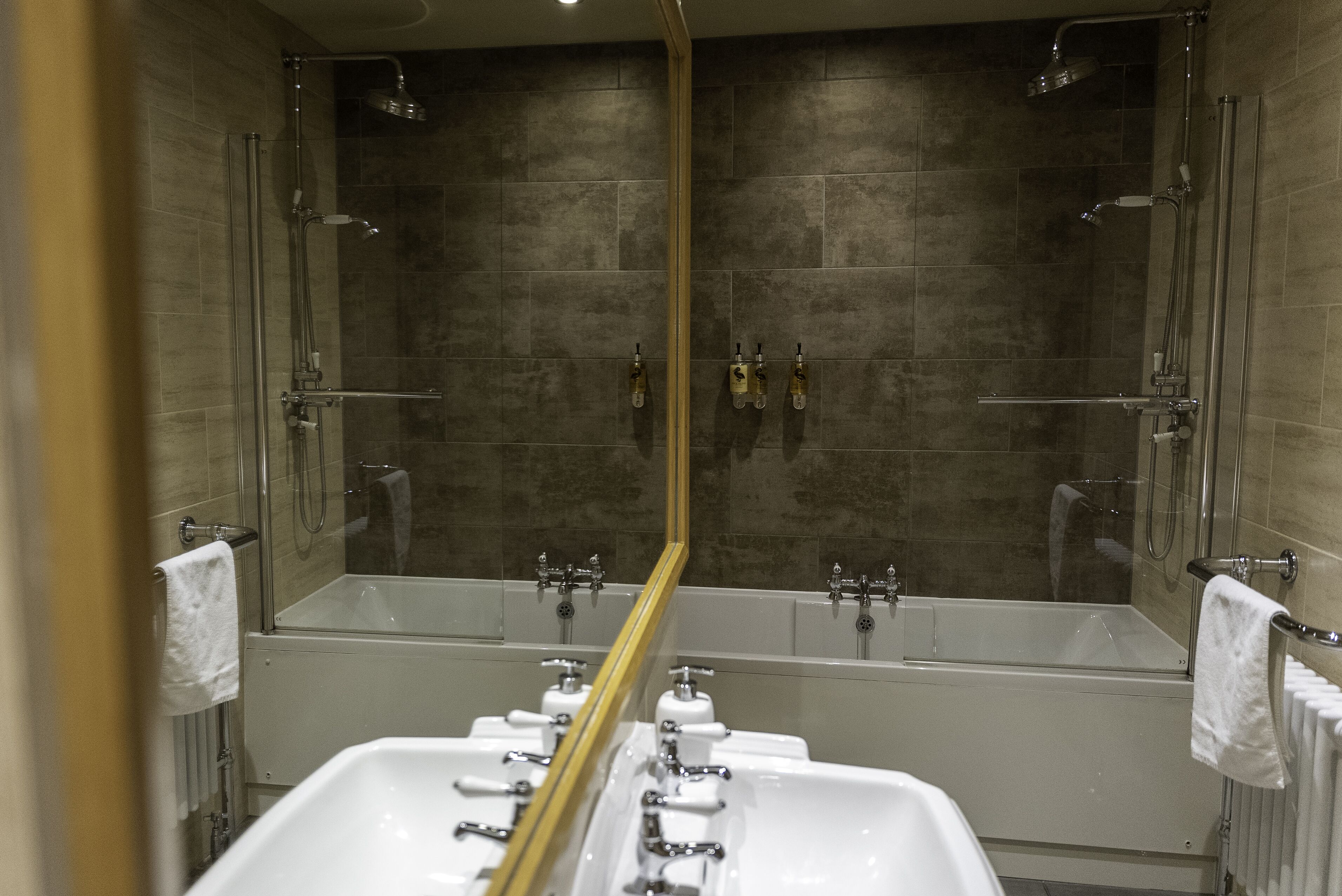 Een moderne badkamer met een grote spiegel, twee wasbakken, een bad en een douche.