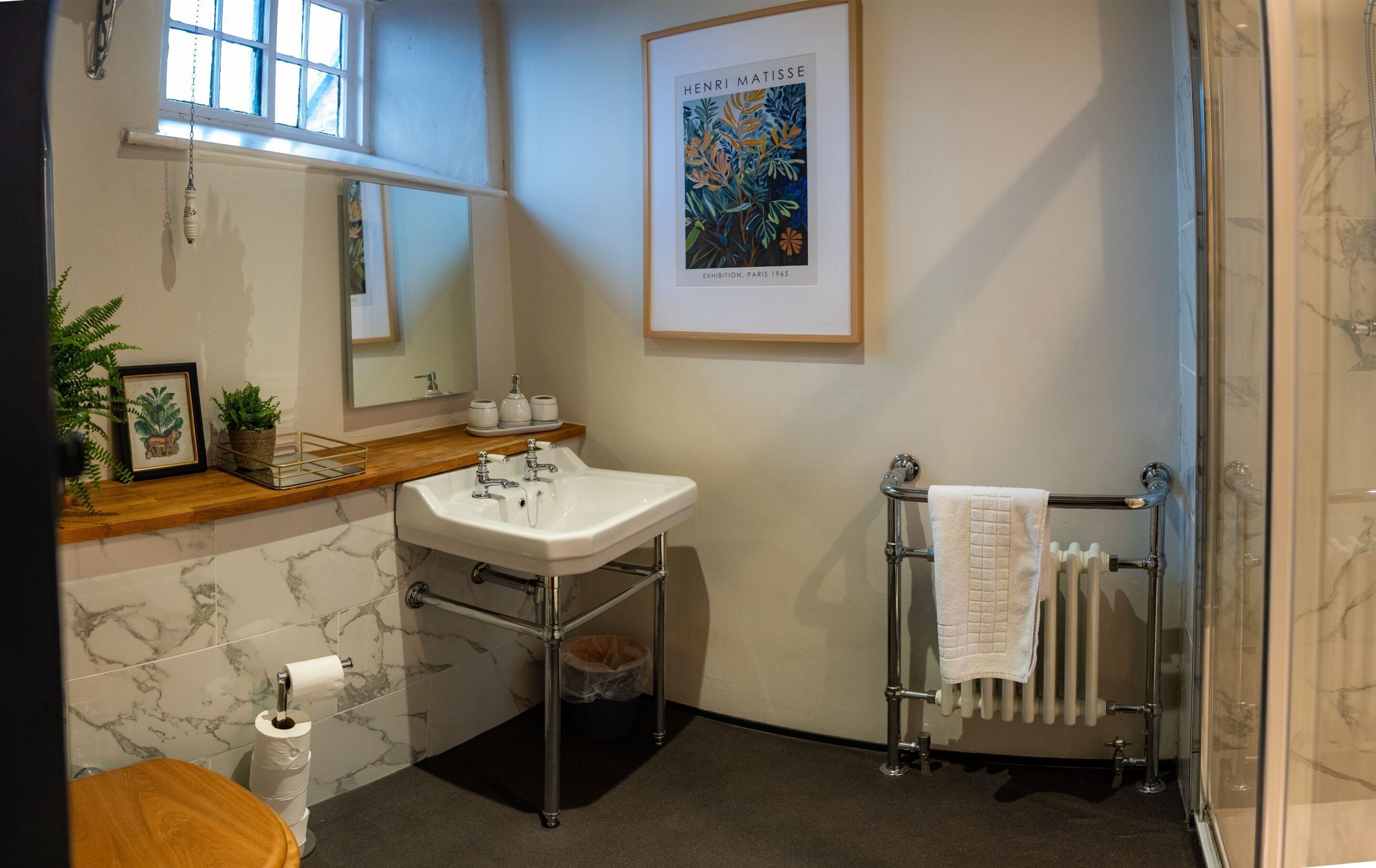 Une salle de bain avec un lavabo en marbre, un plan de toilette en bois, un miroir, une œuvre d’art encadrée, un porte-serviettes et un espace douche.