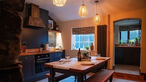 A modern kitchen with dark cabinetry, a wooden dining table set for four, and a large window with curtains. - Duke William Hotel (Lincoln)