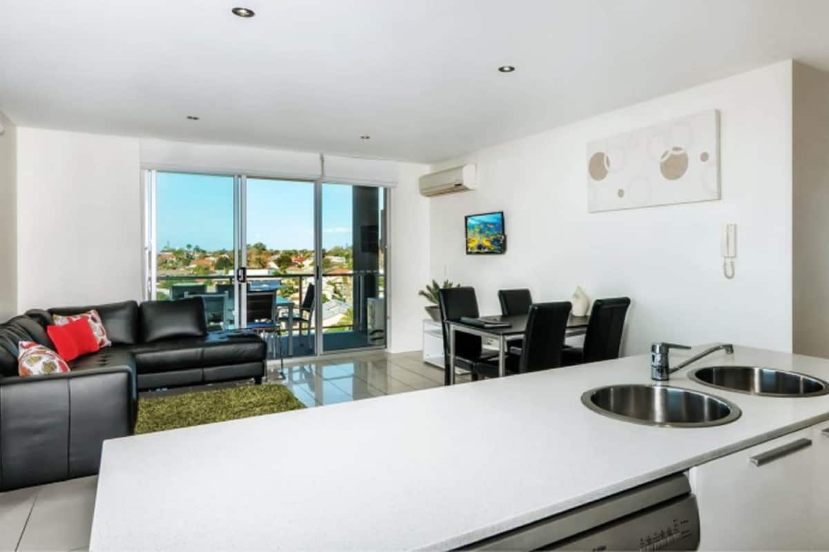A modern kitchen with a large island, dining area, and a living space with a sofa and a balcony.