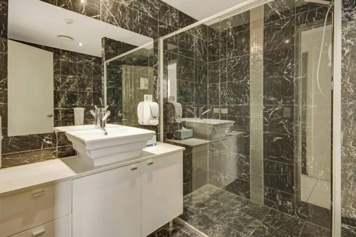 A modern bathroom with a marble sink, a glass shower enclosure, and a large mirror.
