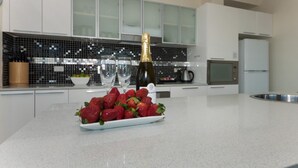 Una cocina moderna con armarios blancos, un salpicadero de azulejos blancos y negros, un lavamanos de acero inoxidable y una encimera con un bol de fresas y una botella de champán.