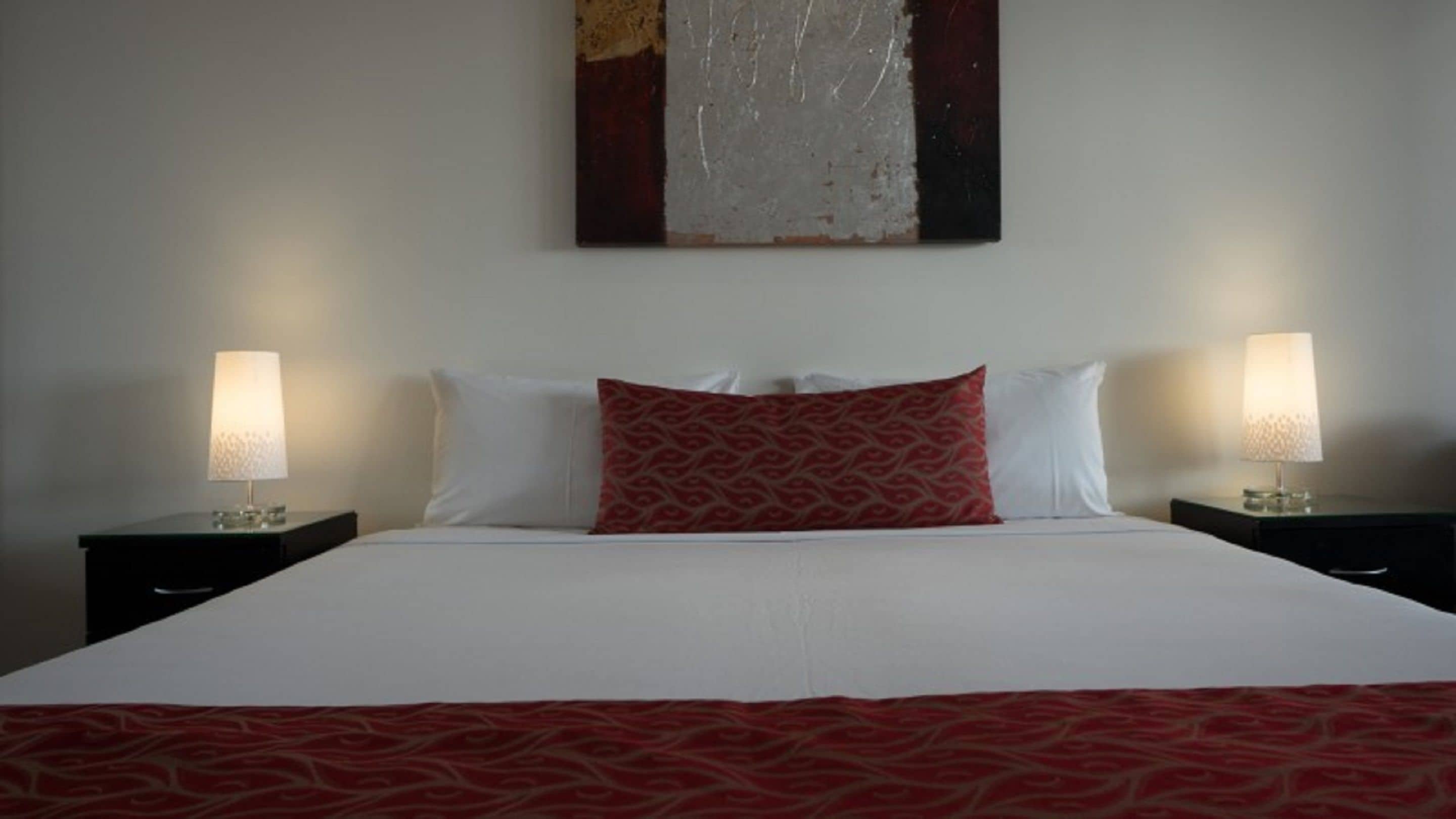 Ein Hotelzimmer mit einem großen Bett, zwei Nachttischen mit Lampen und einer rot gemusterten Tagesdecke.