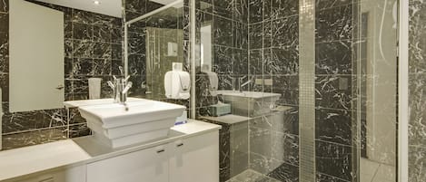 Un baño moderno con lavamanos blanco, espejo y cabina de ducha con mampara de vidrio.