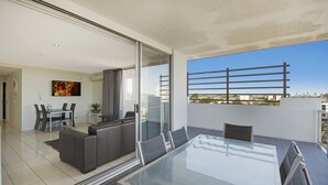 Una sala de estar moderna con una mesa de comedor de vidrio, un sofá gris y vistas a la ciudad a través de amplias ventanas.