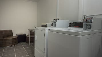 A laundry area with a front-loading washer and dryer, a wicker chair, and a small table.