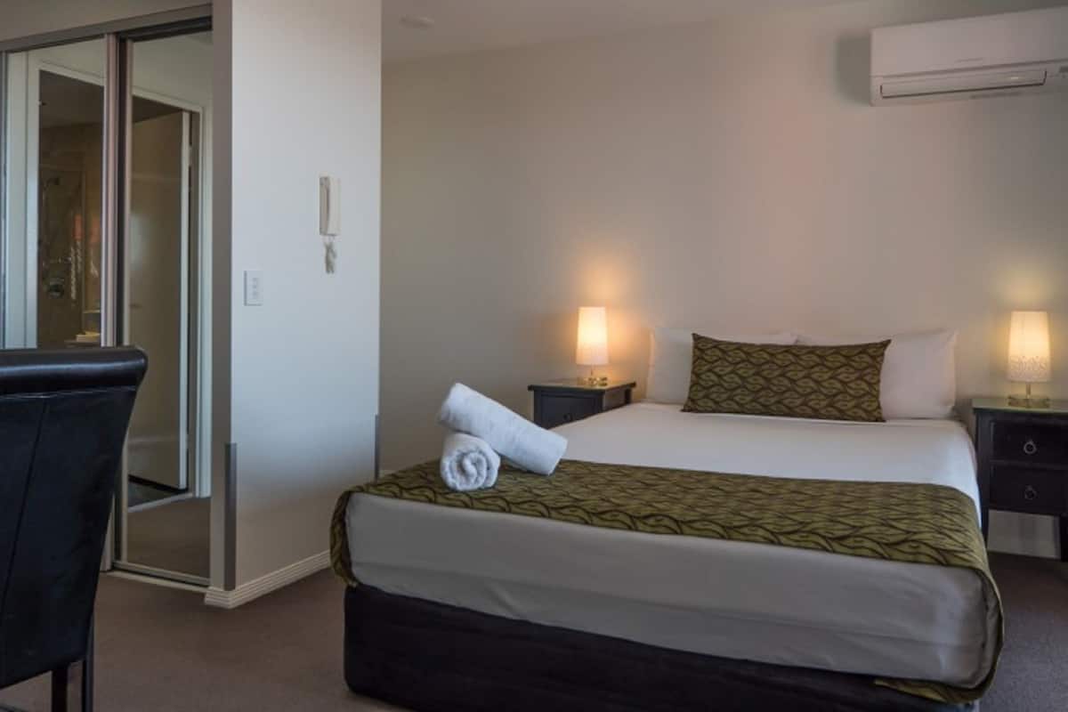 A hotel room with a bed, two bedside tables with lamps, a chair, and an air conditioning unit on the wall.