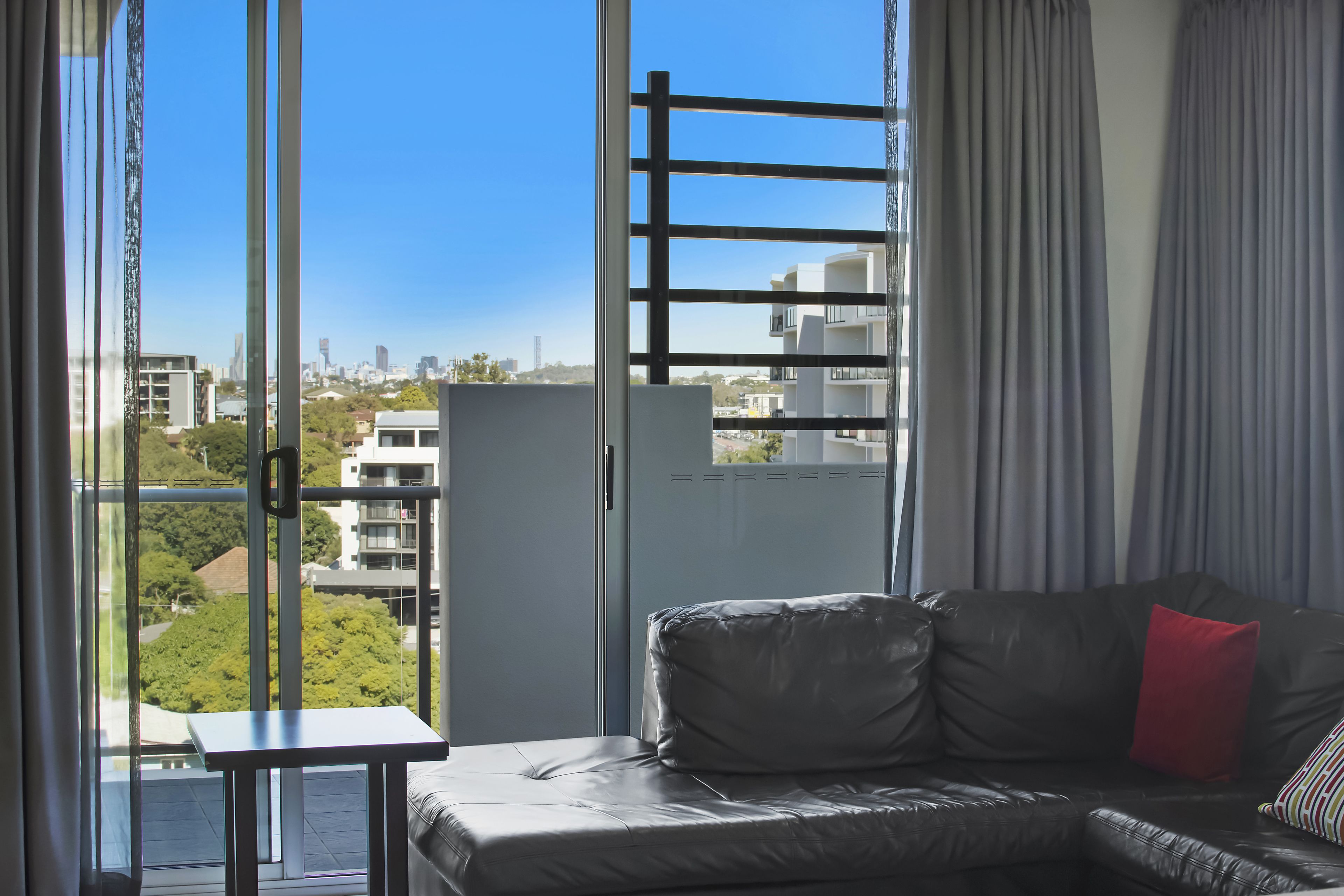 Una sala de estar moderna con un sofá, una mesita y vistas a un paisaje urbano a través de amplios ventanales.