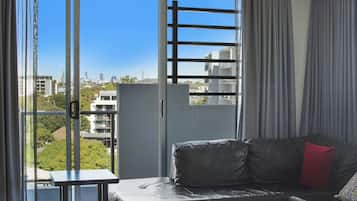 Una sala de estar moderna con un sofá, una mesita y vistas a un paisaje urbano a través de amplios ventanales.