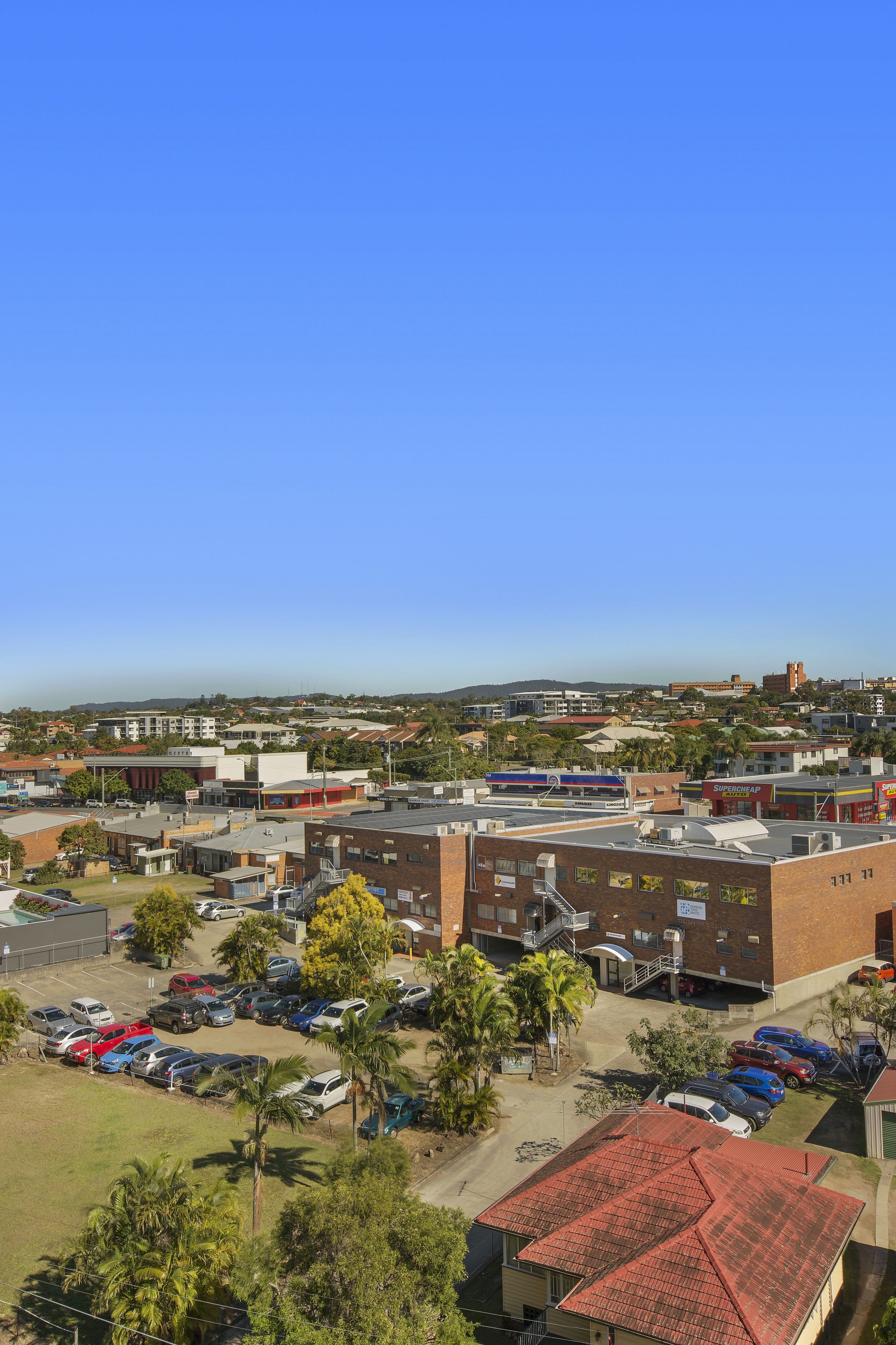 A parking lot with several cars, a building with a red roof, and a clear blue sky.