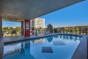 A swimming pool with tiled edges, lounge chairs, and a view of a multi-story building in the background. - The Chermside Apartments (Chermside)