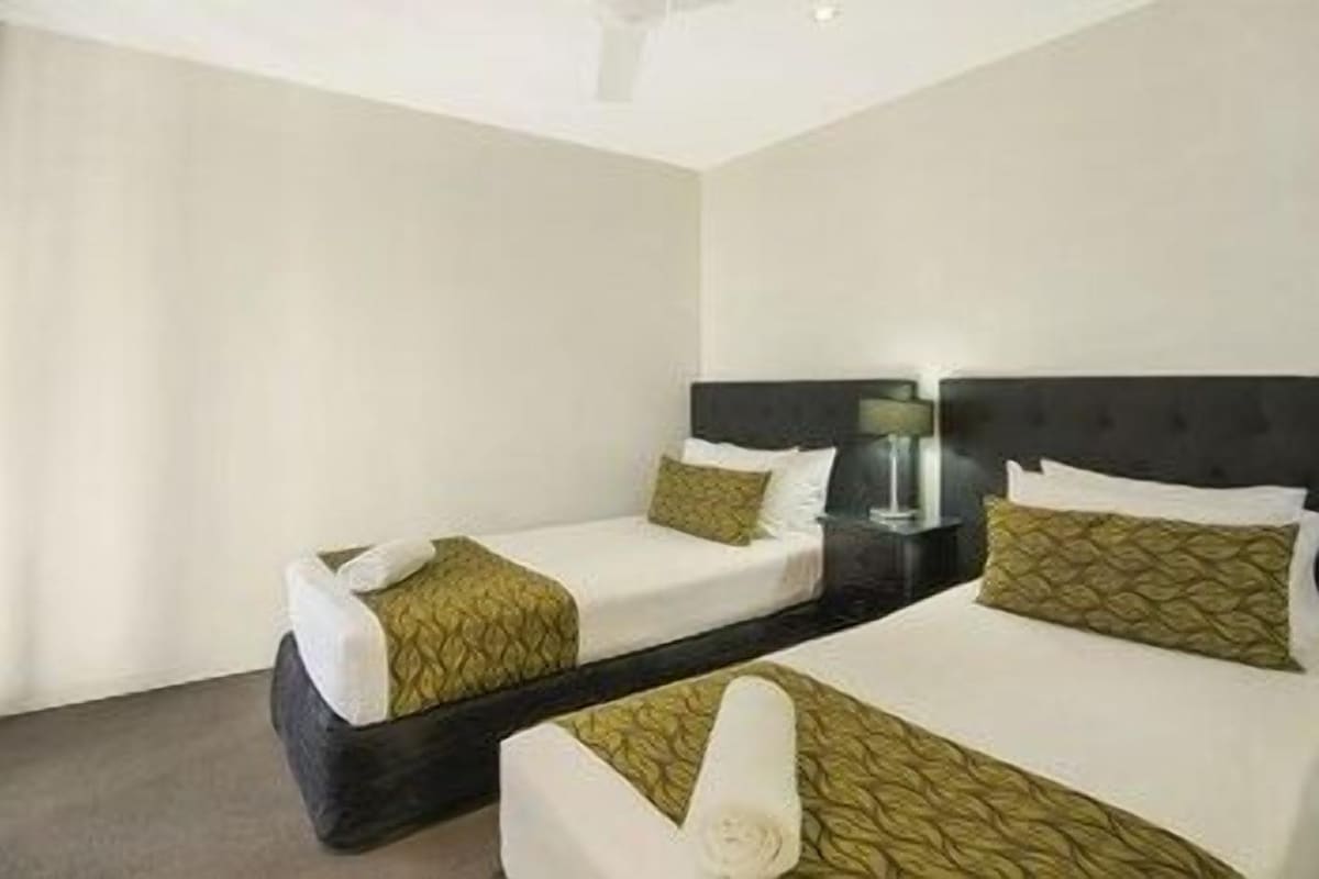 A hotel room with two single beds, a bedside table with a lamp, and a large window.