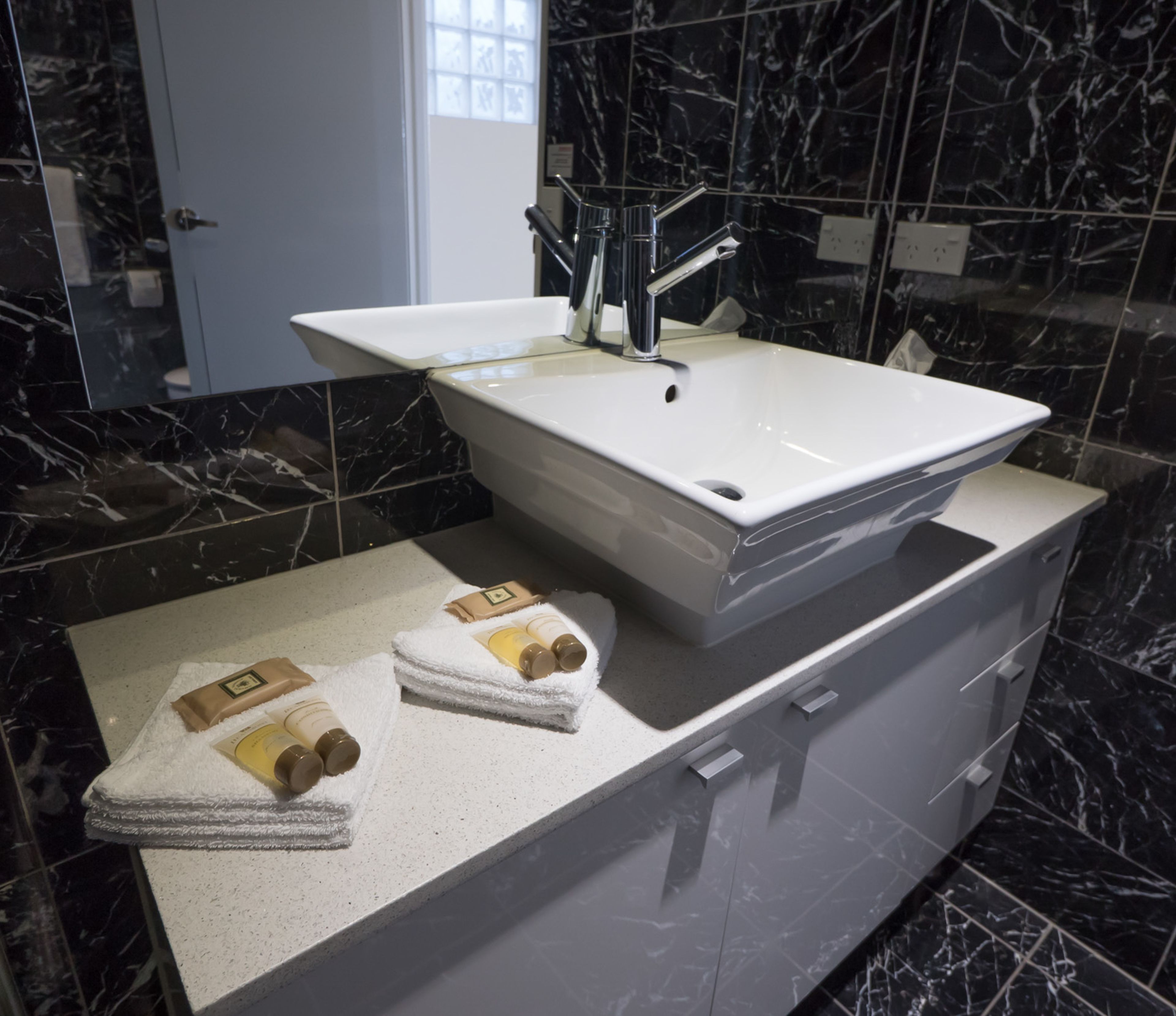 Een badkamer met een wit wastafelmeubel, zwarte marmeren tegels en twee handdoeken op het aanrecht.
