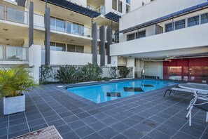 A modern building with a swimming pool, outdoor seating, and a well-maintained garden. - The Chermside Apartments (Chermside)