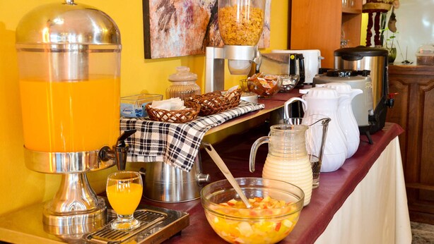 Montaje de desayuno buffet con dispensador de zumo, cereales y diversas opciones de comida.