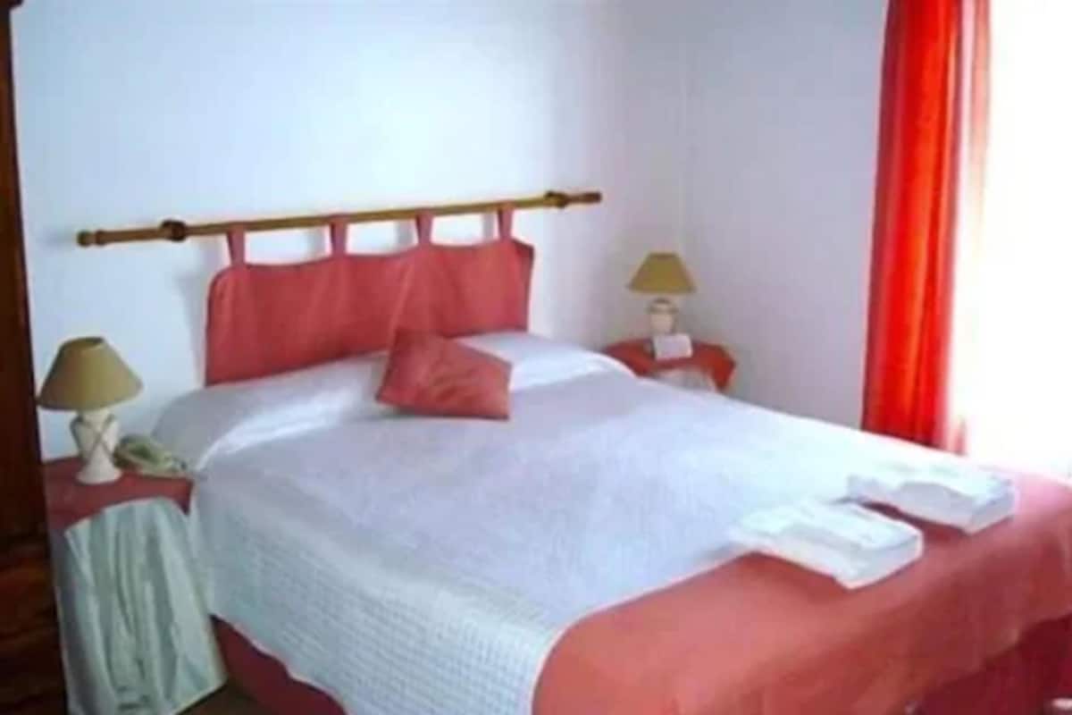 Une chambre d’hôtel standard, avec un lit, deux tables de chevet, une lampe et un rideau rouge.