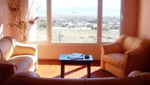 Un salón con sofá, una mesa de centro y vistas a un paisaje a través de amplios ventanales.