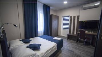 Habitación de hotel con cama, escritorio, silla y ventana con persianas.