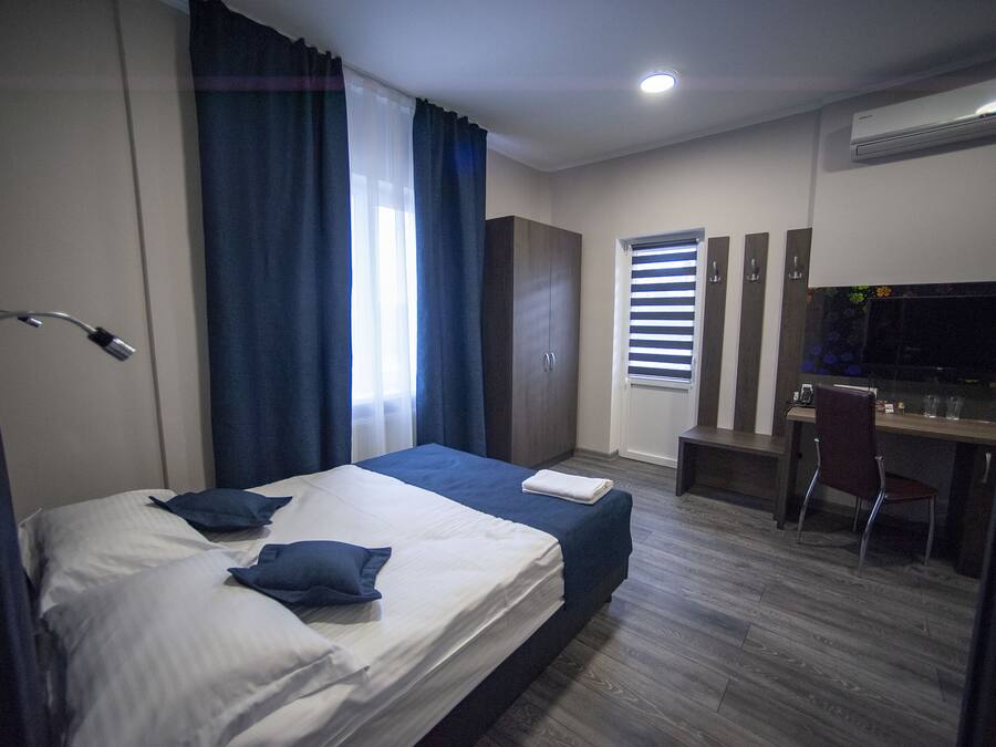 Habitación de hotel con cama, escritorio, silla y ventana con persianas.