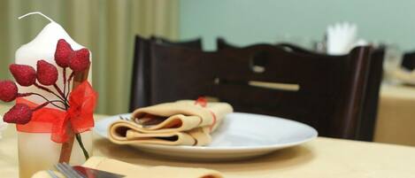 Una mesa dispuesta con una servilleta doblada, un plato con servilletas enrolladas y una vela adornada con un lazo y bayas rojas.