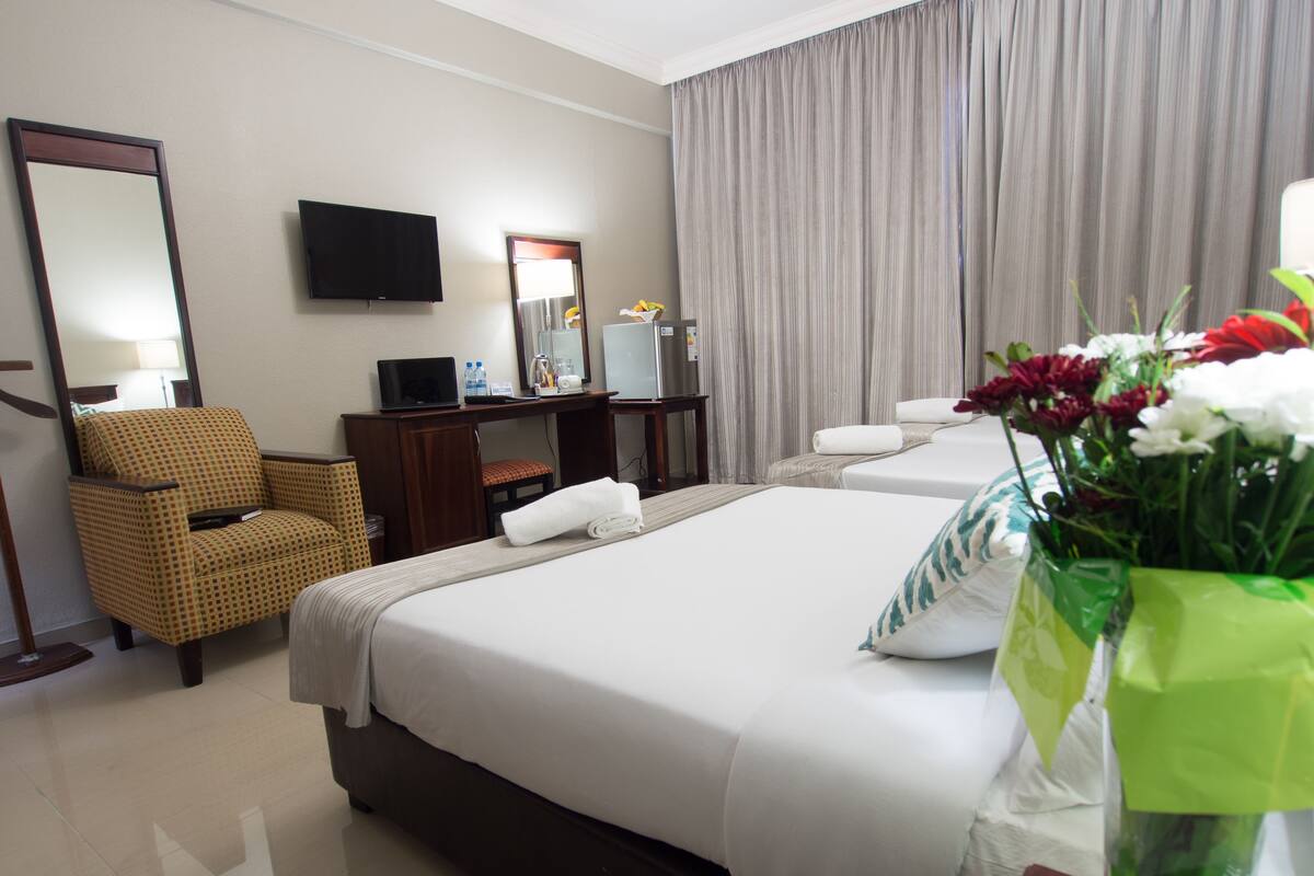 Een hotelkamer met een groot bed, een bureau met een computer, een stoel, een televisie en een raam met gordijnen.