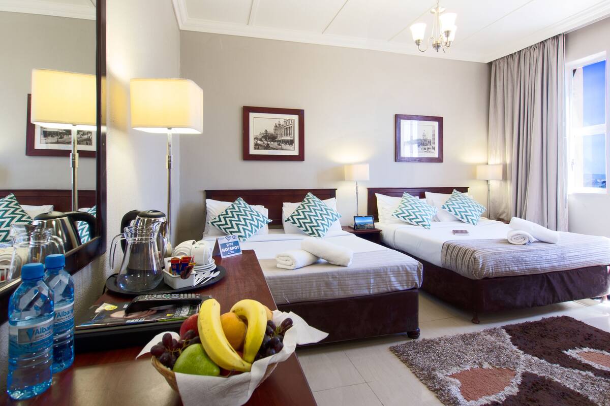 Een hotelkamer met twee bedden, een bureau met een laptop, een fruitmand en een minibars.
