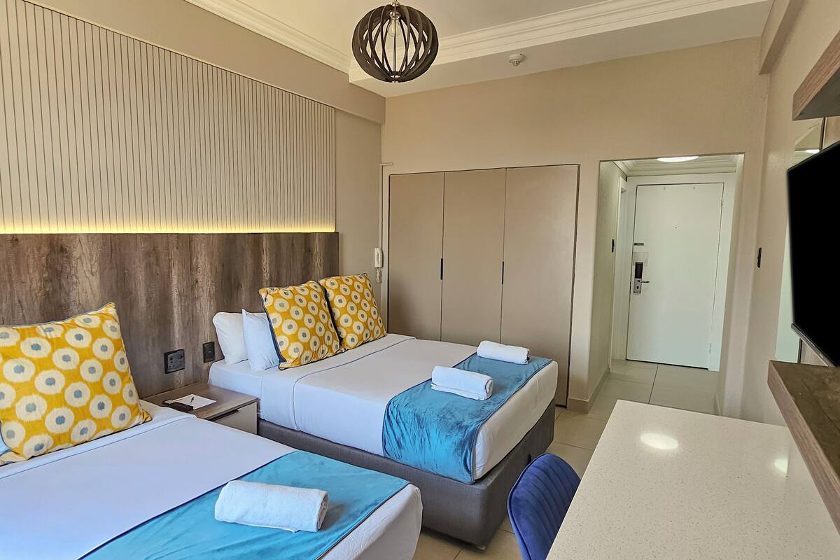 Een hotelkamer met twee bedden, een bureau, een stoel, een televisie en een kledingkast.