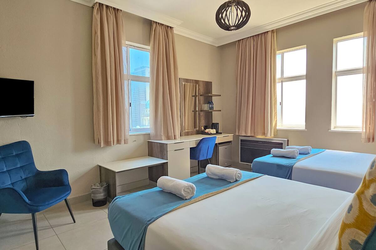Een hotelkamer met twee bedden, een bureau, een stoel, een televisie en een raam met gordijnen.