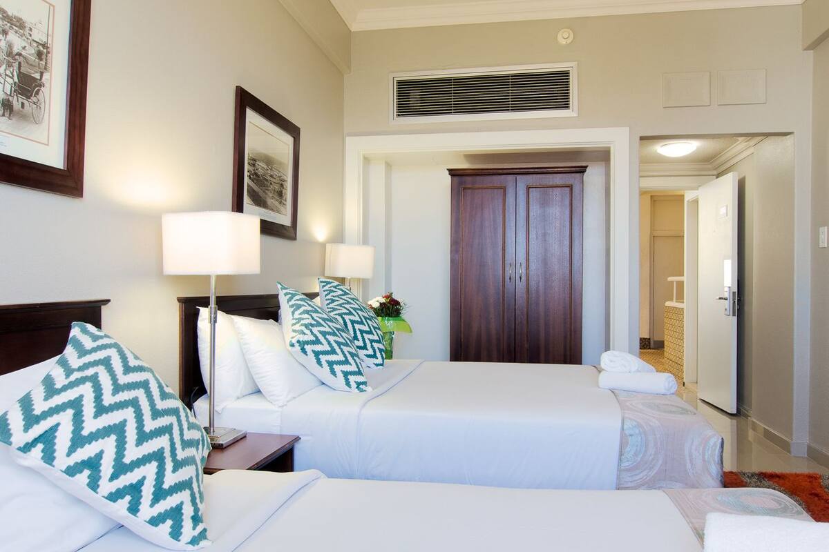 Een hotelkamer met twee bedden, een kroonluchter, ingekaderde foto's aan de muur en een deur naar een andere kamer.