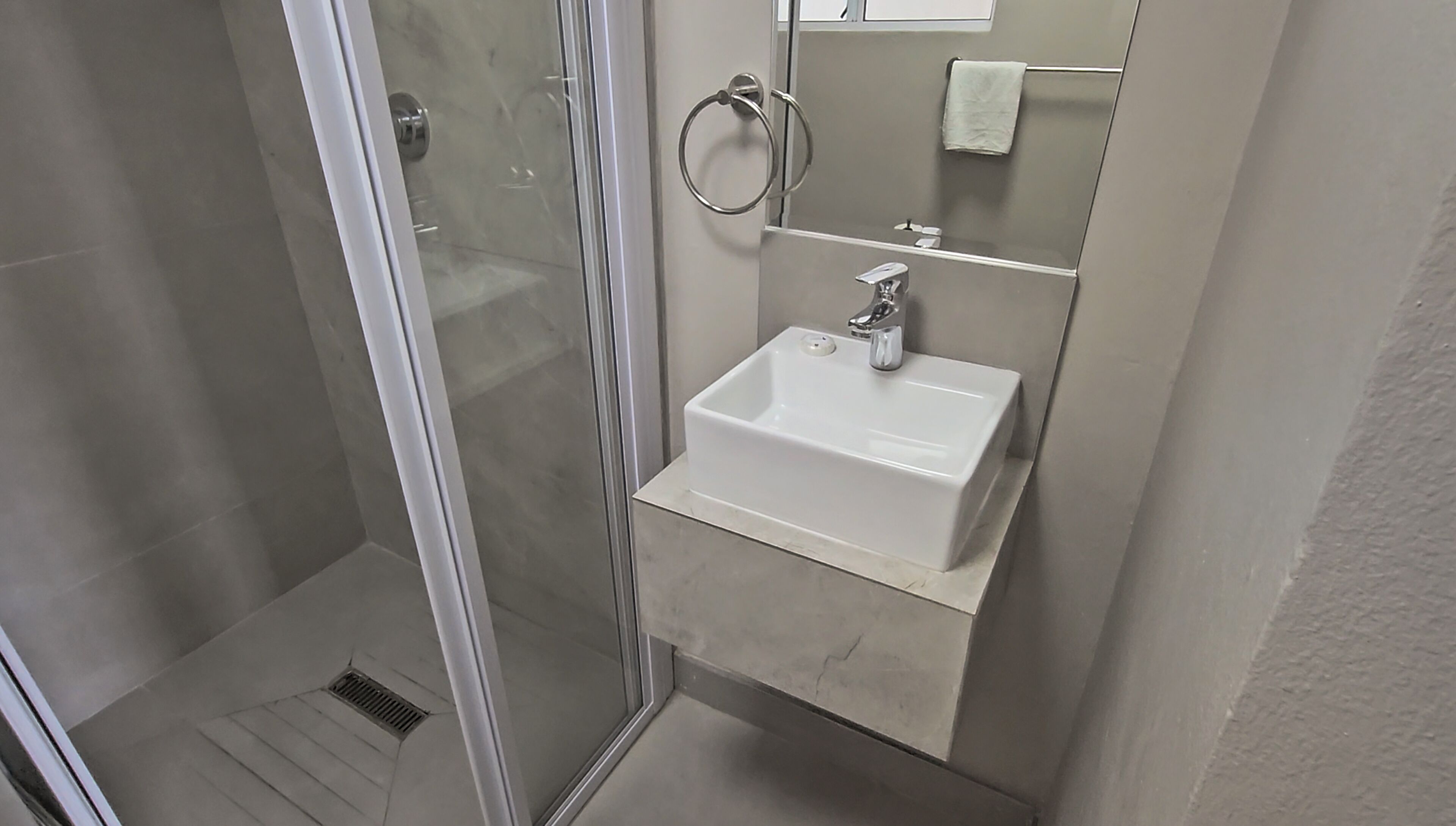 A bathroom with a glass shower enclosure, a white sink, and a mirror.