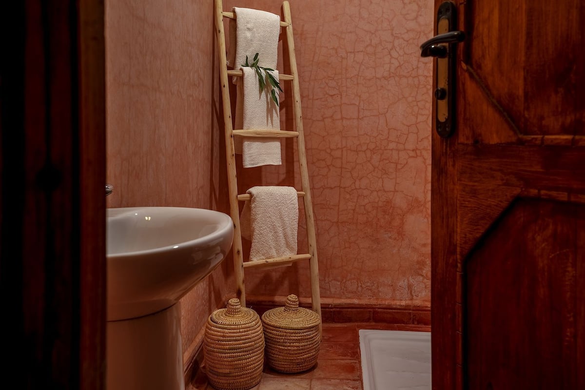 Une salle de bain avec une échelle en bois, un lavabo et deux paniers en osier.