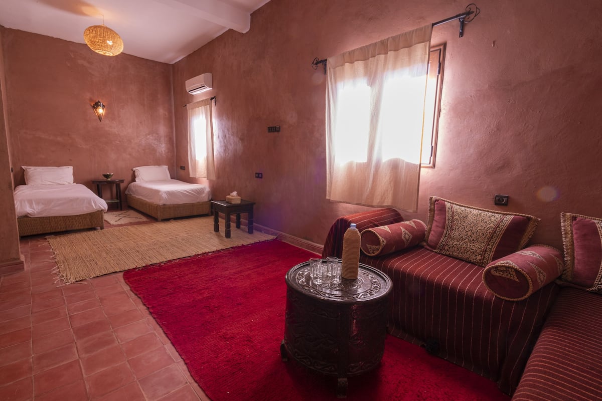 Une chambre avec deux lits, un tapis rouge, une table ronde avec une bougie et un canapé à rayures.
