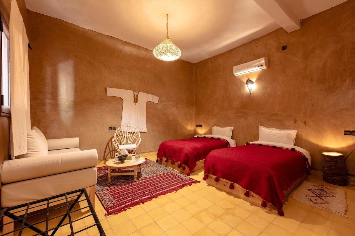 Une pièce comprenant deux lits, un canapé, une petite table, un lustre et un luminaire fixé au mur.