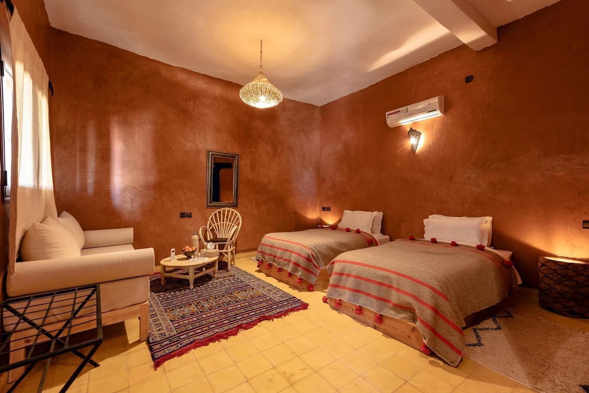 Une chambre avec deux lits, une chaise, une petite table, un luminaire suspendu et un appareil de climatisation.