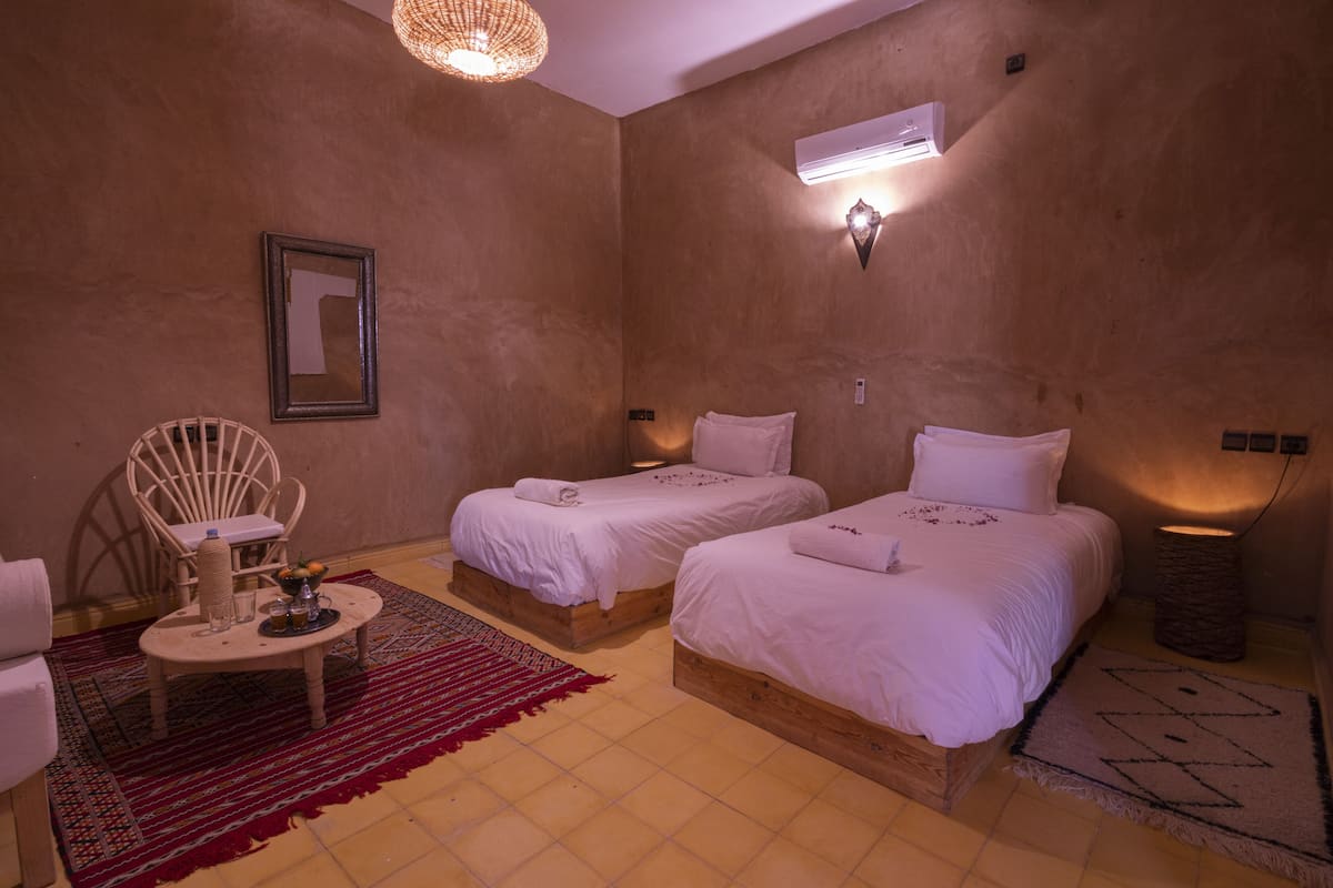 Une pièce confortable avec deux lits, une chaise, une petite table et un tapis rouge.