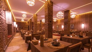 Ein Restaurant mit Steinsäulen, gedeckten Tischen mit Kerzen und warmer Beleuchtung.