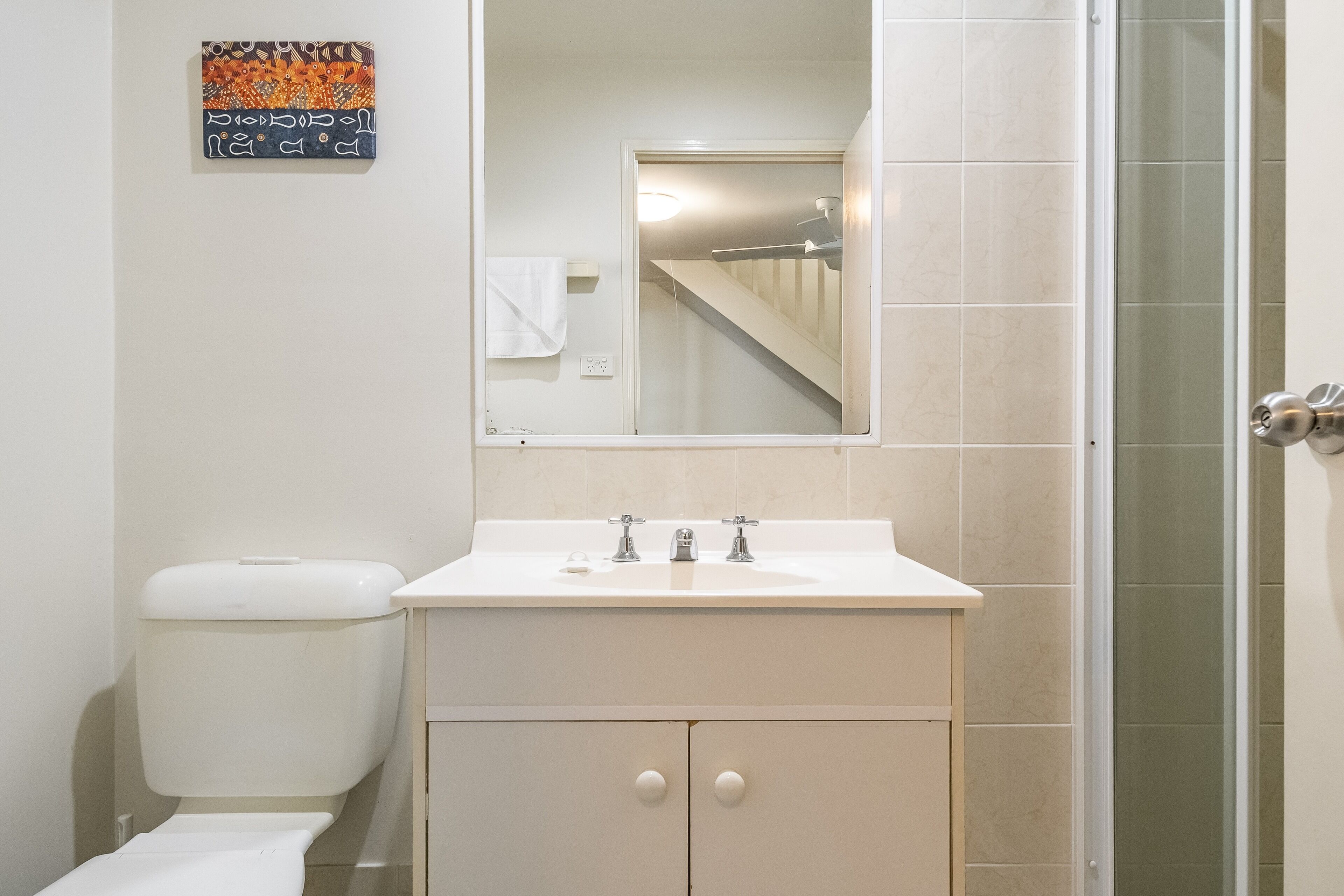A bathroom with a white sink, two faucets, a mirror above the sink, a toilet, and a shower area.