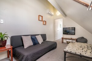 Una sala de estar moderna con un sofá gris oscuro, una mesa de centro estampada, un televisor de pantalla plana y un banco de madera.