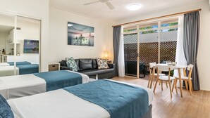 A hotel room with two beds, a sofa, a dining table with chairs, a ceiling fan, and a view through a sliding glass door. - Byron Central Apartments (Byron Bay)