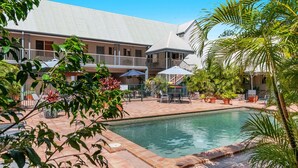A pool area with a tiled deck, surrounded by potted plants and outdoor furniture. - Byron Central Apartments (Byron Bay)