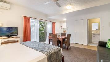 Habitación de hotel con cama, televisor, mesa de comedor, sillas y balcón con cortinas.