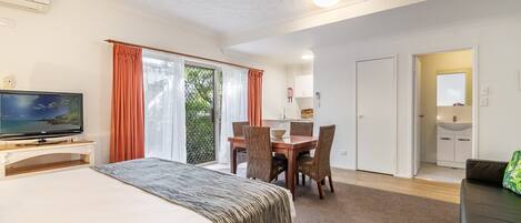 Habitación de hotel con cama, televisor, mesa de comedor, sillas y balcón con cortinas.