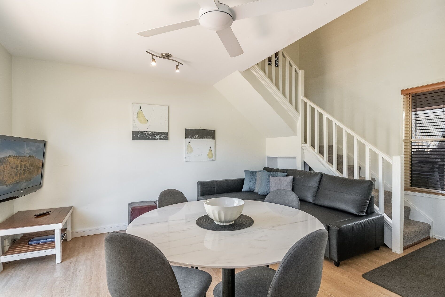 A modern living room with a dining table, grey sofa, and a ceiling fan.