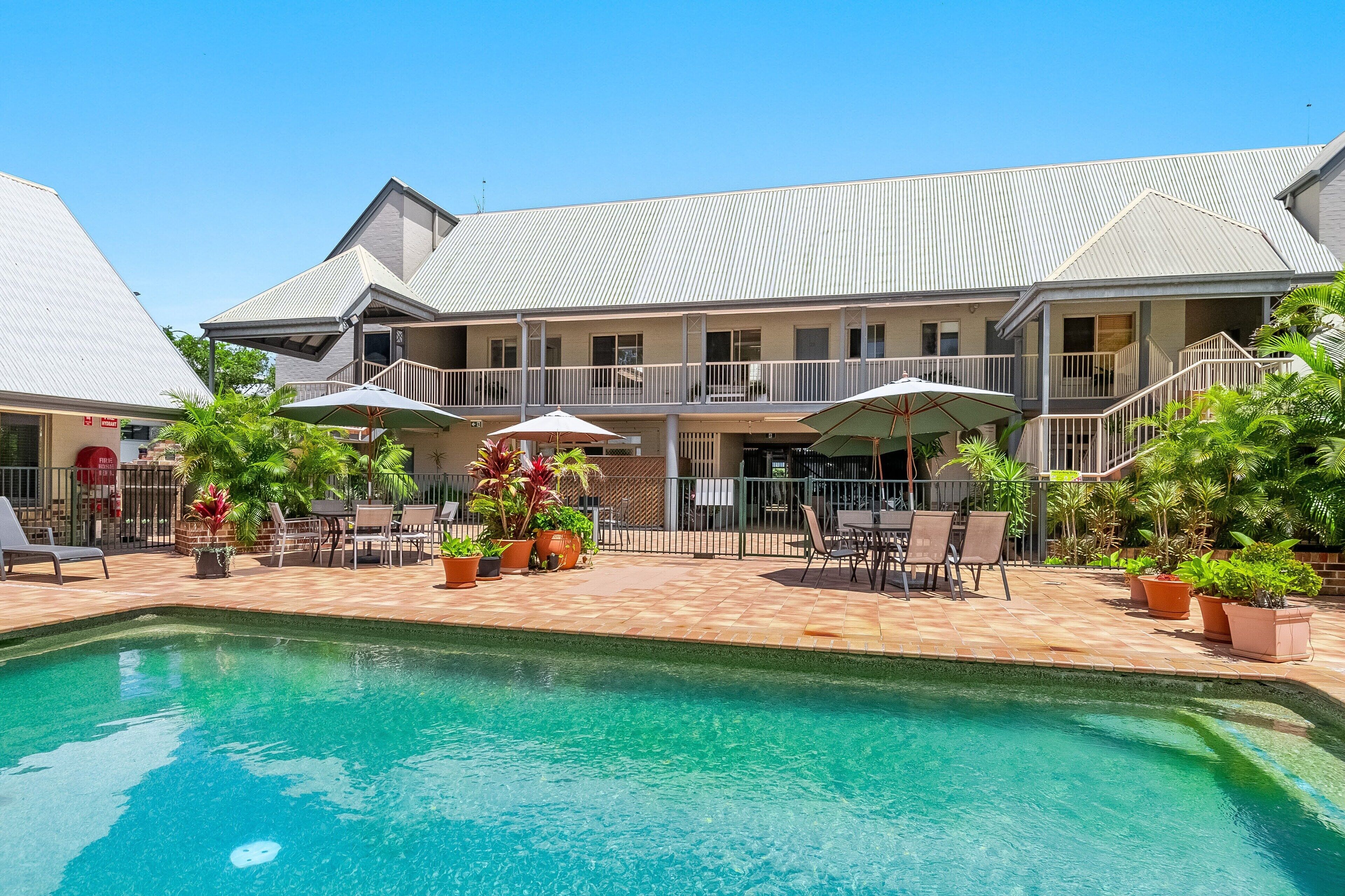 A hotel with a swimming pool, outdoor seating, and a covered patio area.